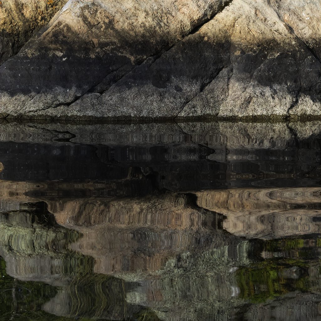 Layers of colour in granite rock reflected in the water below